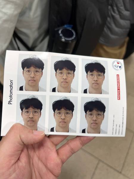 역 안 포토부스에서 찍은 증명사진 6장을 손에 들고 있는 모습. 약간 멍한 표정