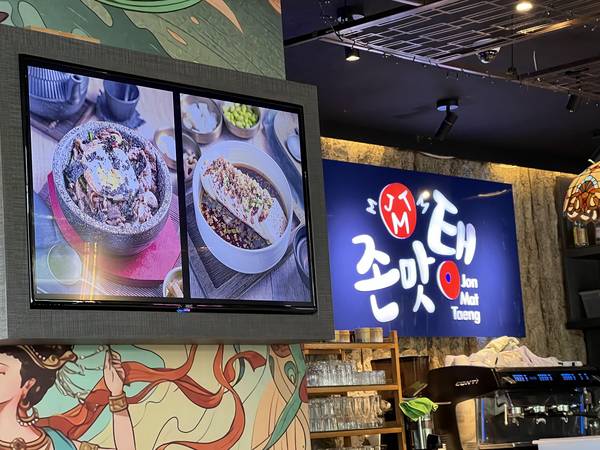 '존맛탱' 한국 식당 내부. TV 화면에 한국 음식 사진이 나오고 있고, 간판에 '존맛탱 JonMatTang'이라고 적혀있다. 벽면에 일러스트 벽화