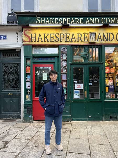 셰익스피어 앤 컴퍼니 서점 앞에서 포즈를 취한 모습. 초록색 서점 간판과 노란 'SHAKESPEARE AND COMPANY' 글씨가 보인다