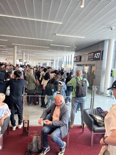 오를리 공항 게이트 앞. 승객들이 짐을 놓고 바닥에 앉아 있다. 전광판에 게이트 번호가 보인다. 지친 표정의 사람들