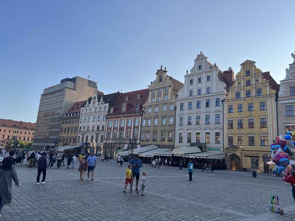 브로츠와프 리넥 광장(Rynek). 넓은 광장 주변으로 다채로운 색상의 타운하우스들이 늘어서 있다. 관광객들이 걸어다니고, 풍선 파는 사람도 보인다. 저녁 햇살