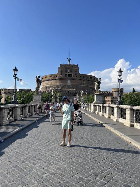 성천사성(Castel Sant'Angelo). 원형 성 건물이 파란 하늘 아래 우뚝 서 있고, 다리 위에 사람들이 걸어가고 있다
